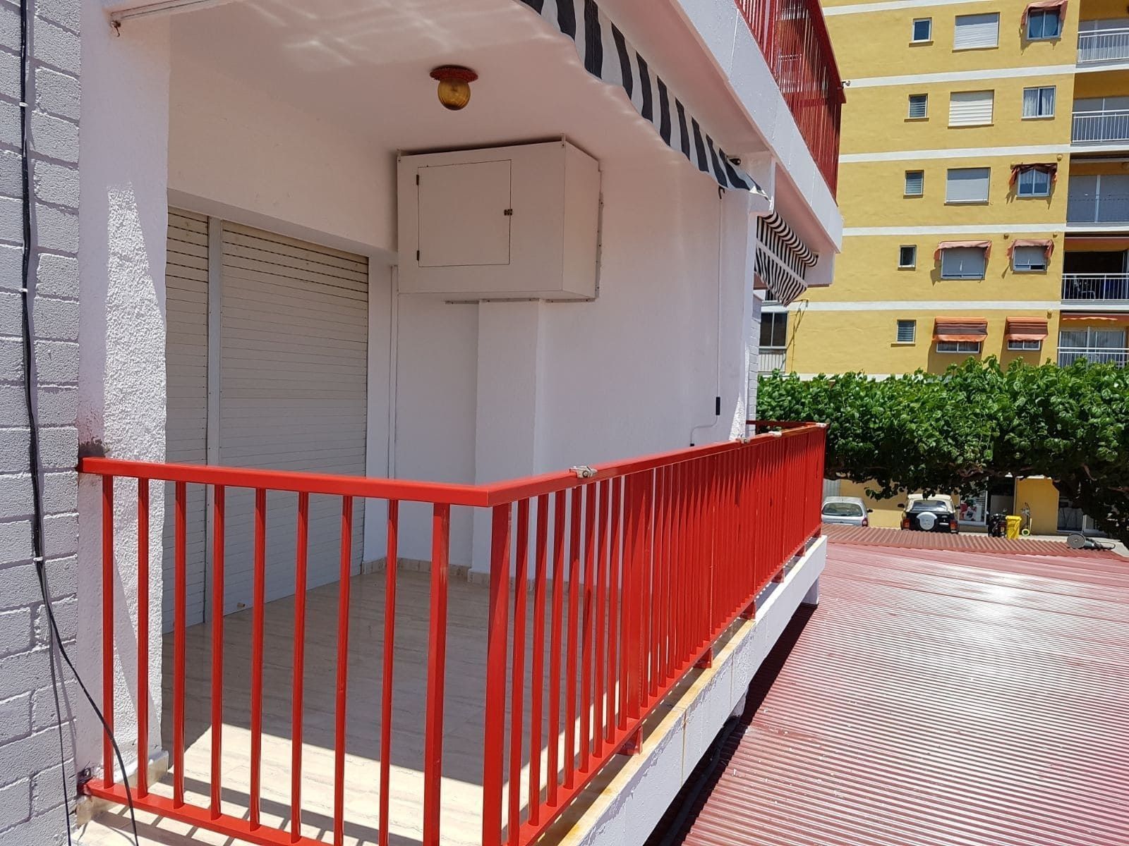 Pasarela con barandilla roja junto a un edificio blanco y un patio pavimentado en un complejo de apartamentos.