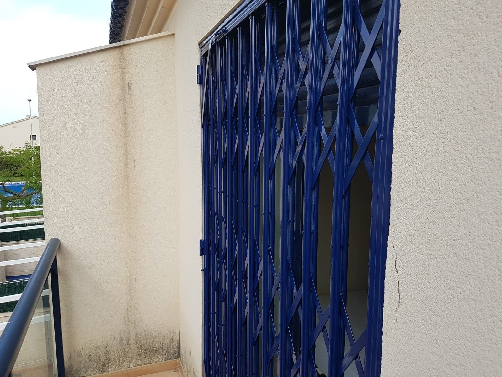 Puerta de metal azul junto a una pared beige en un estrecho pasillo exterior.