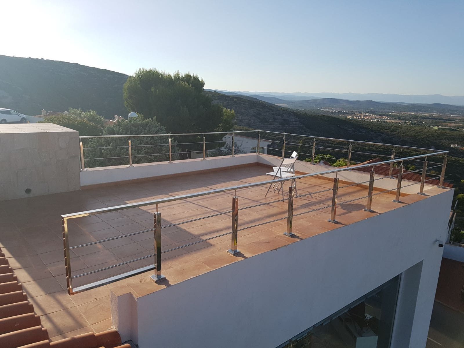 Terraza en la azotea con tarima de madera, barandilla de metal y vistas a la montaña bajo un cielo despejado.