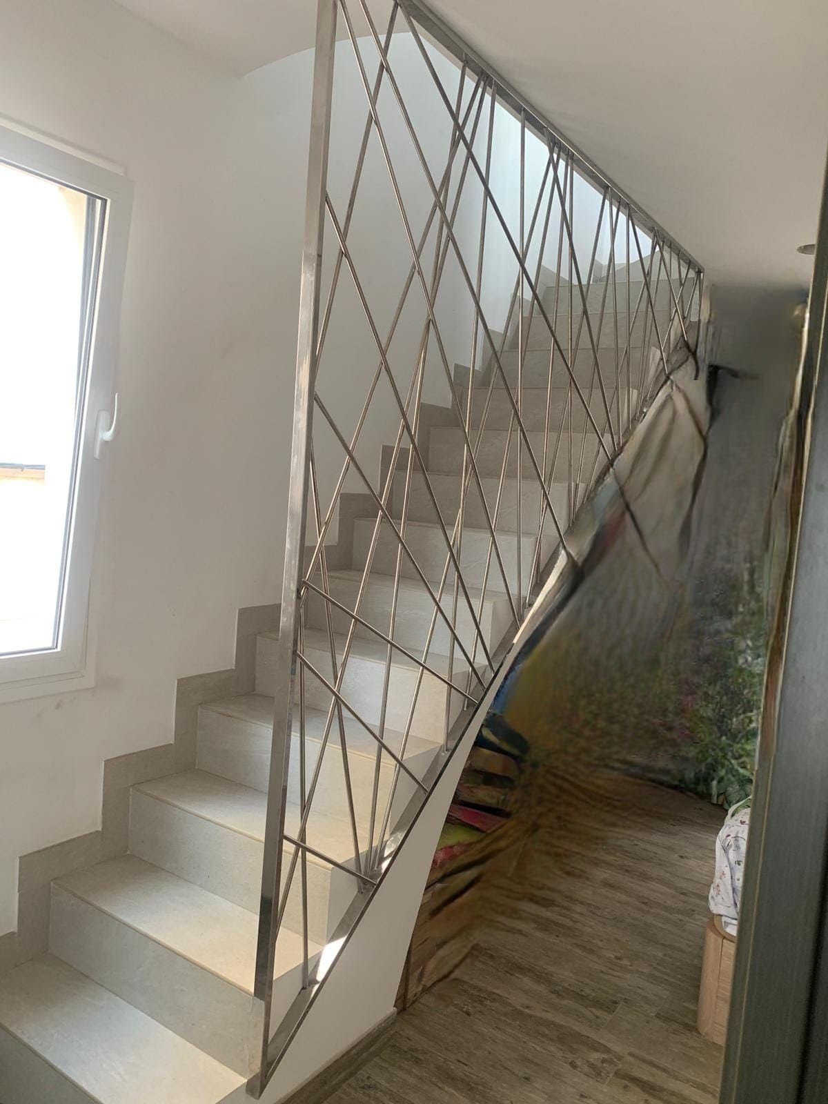 Escalera con paredes blancas, barandilla metálica geométrica y suelo de madera clara que conduce a la planta superior.