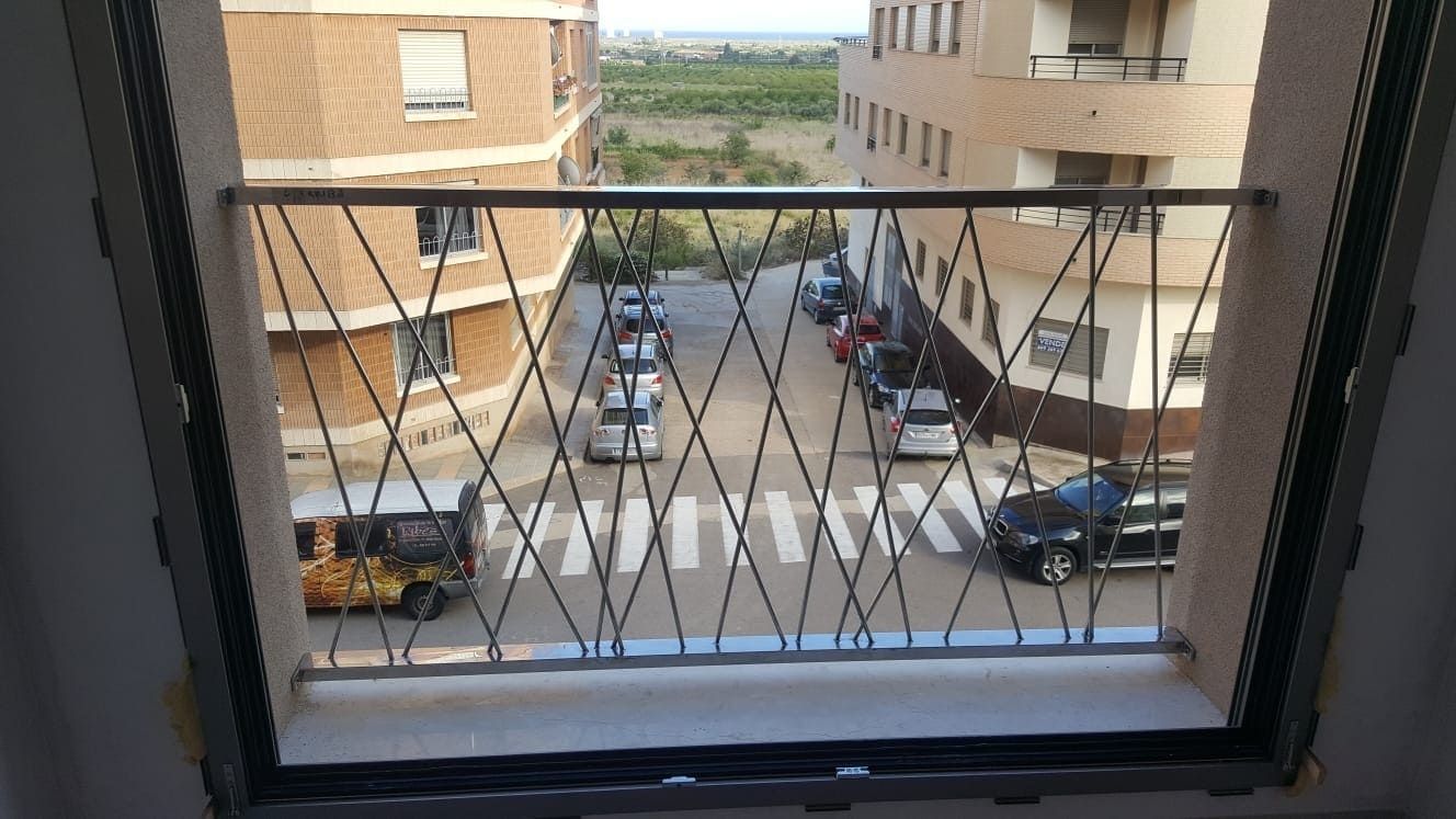 Vista desde una ventana de edificios de apartamentos y coches aparcados a lo largo de una estrecha calle con patio interior.
