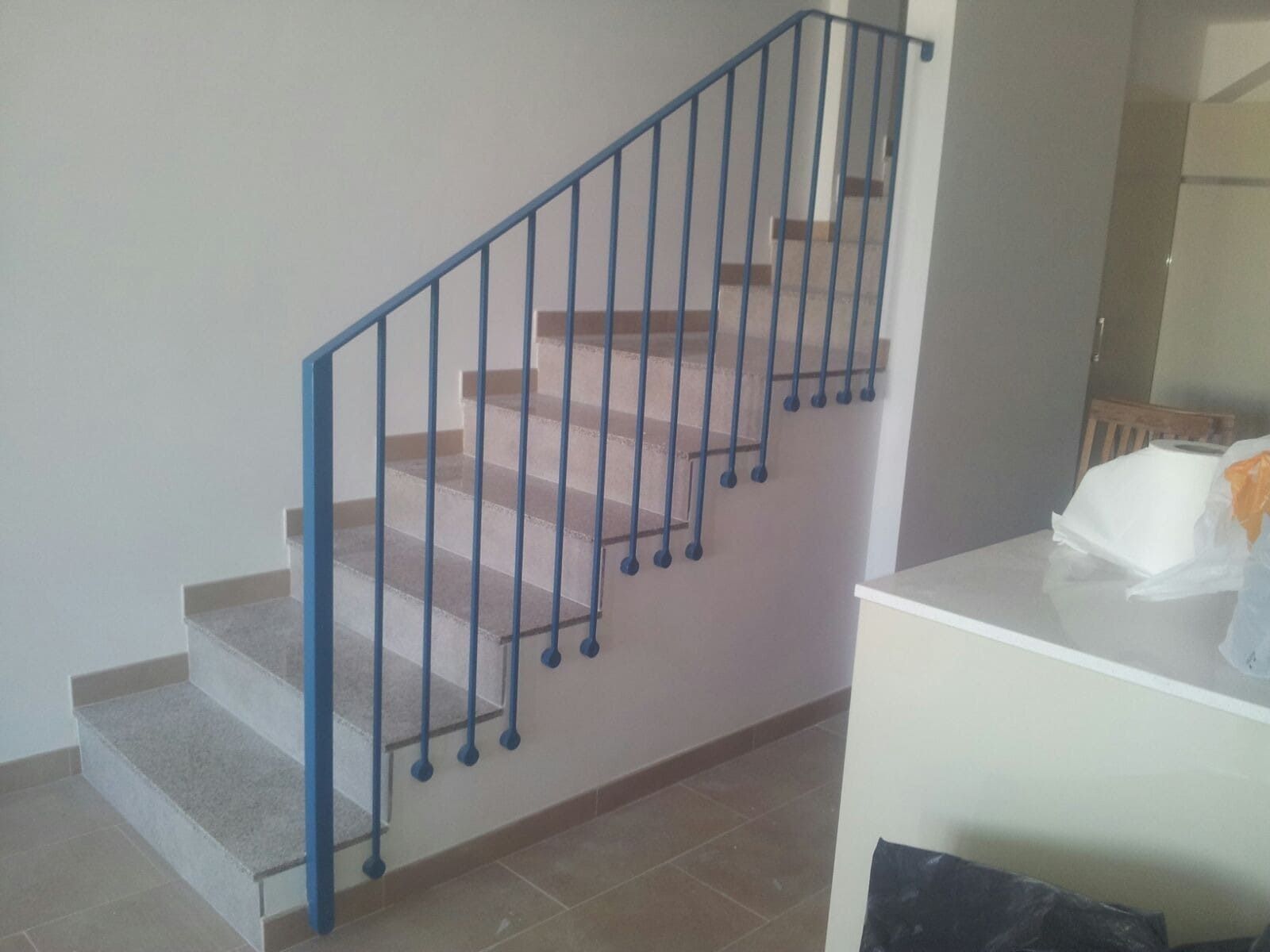 Escalera interior con escalones alfombrados de rosa, barandilla de metal azul y paredes beige.