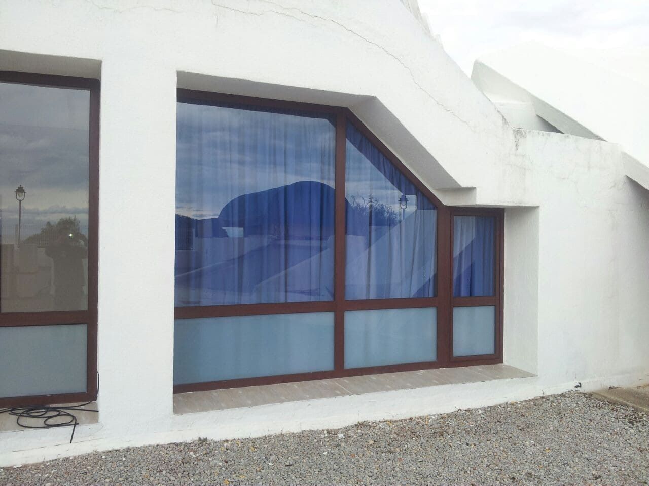 Edificio de fachada blanca con grandes ventanas de tonos azules y suelo de grava.