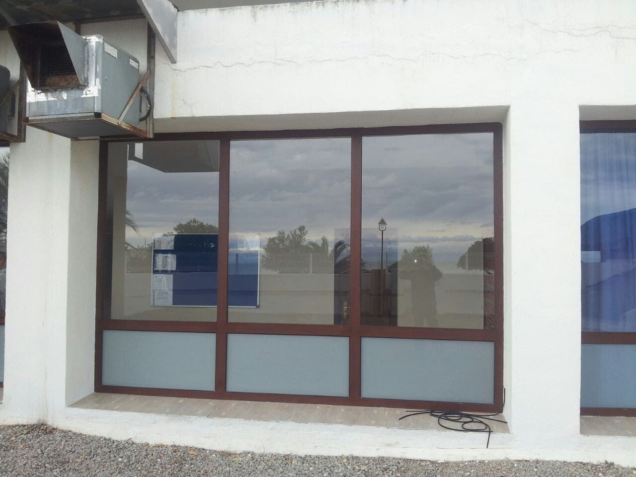 Escaparate reflectante con marco marrón sobre fachada blanca.