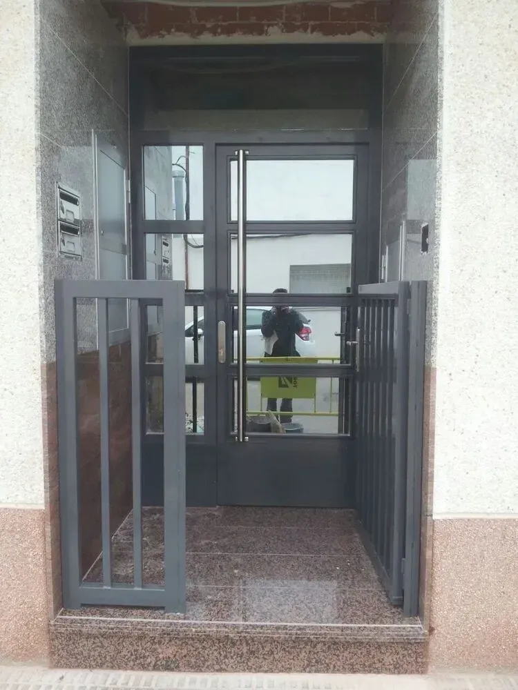 Vestíbulo de entrada con puertas de cristal abiertas y una persona de pie a lo lejos en el exterior.