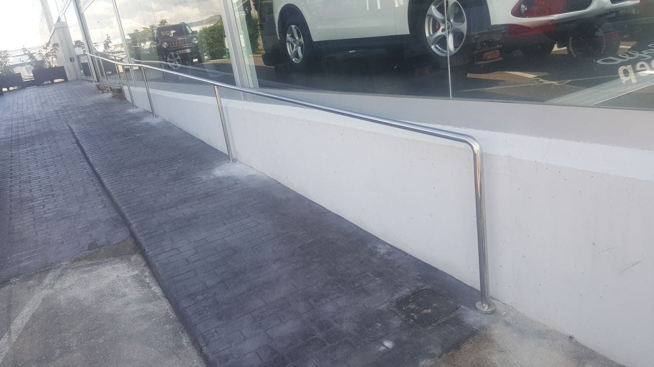 Rampa de acceso de hormigón junto al escaparate de una tienda, con los coches aparcados reflejados en el cristal.