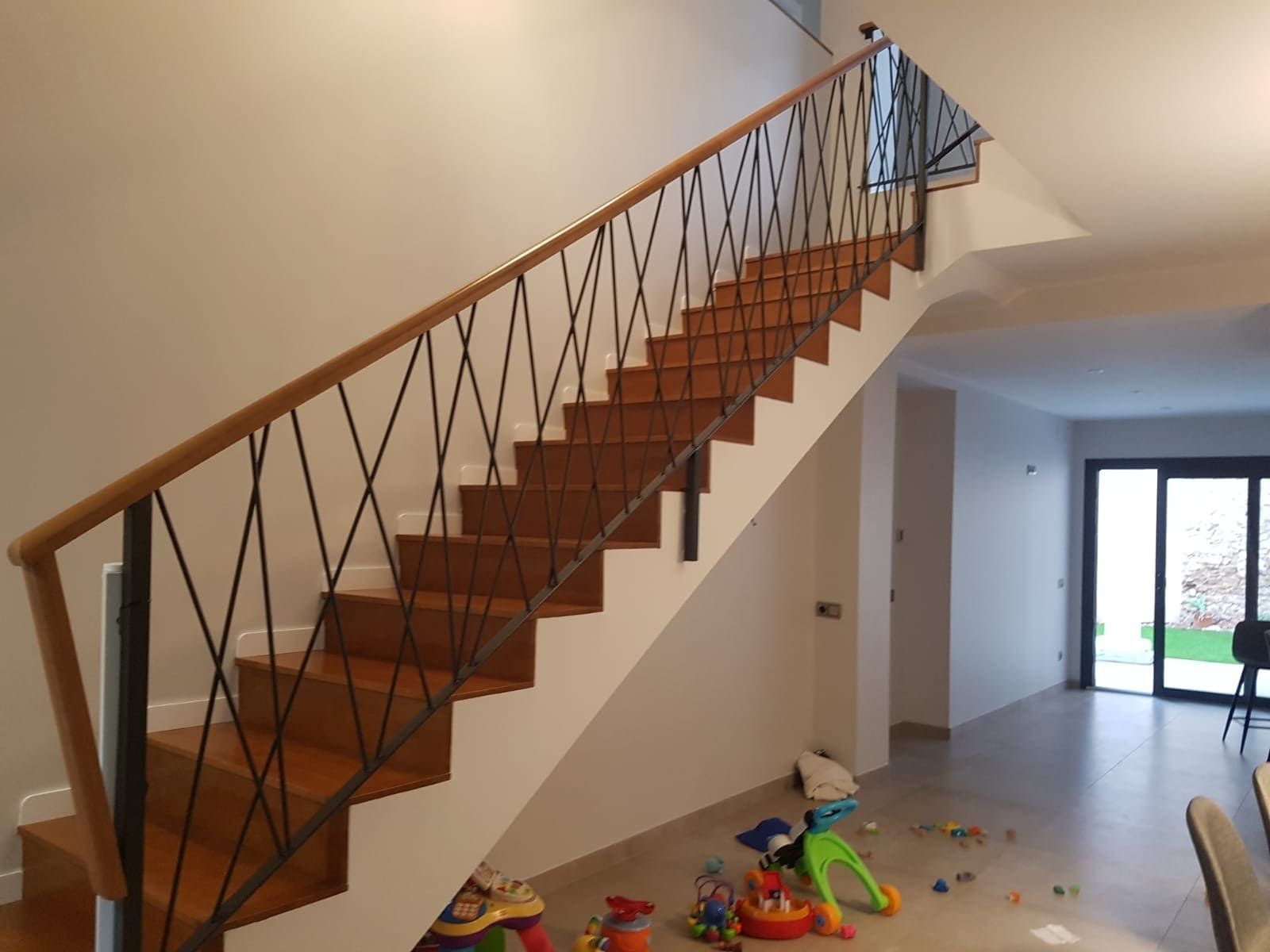 Escalera interior con peldaños y barandilla de madera en una habitación luminosa y vacía, con juguetes esparcidos por el suelo.