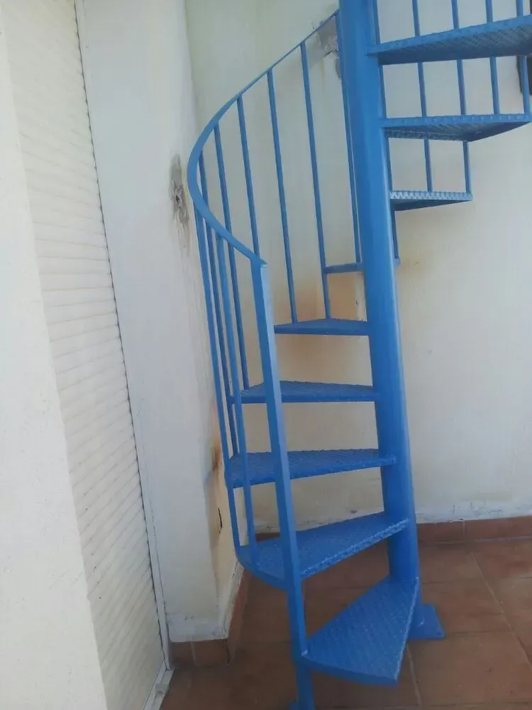 Escalera de caracol azul en un pequeño espacio interior con suelo de baldosas.