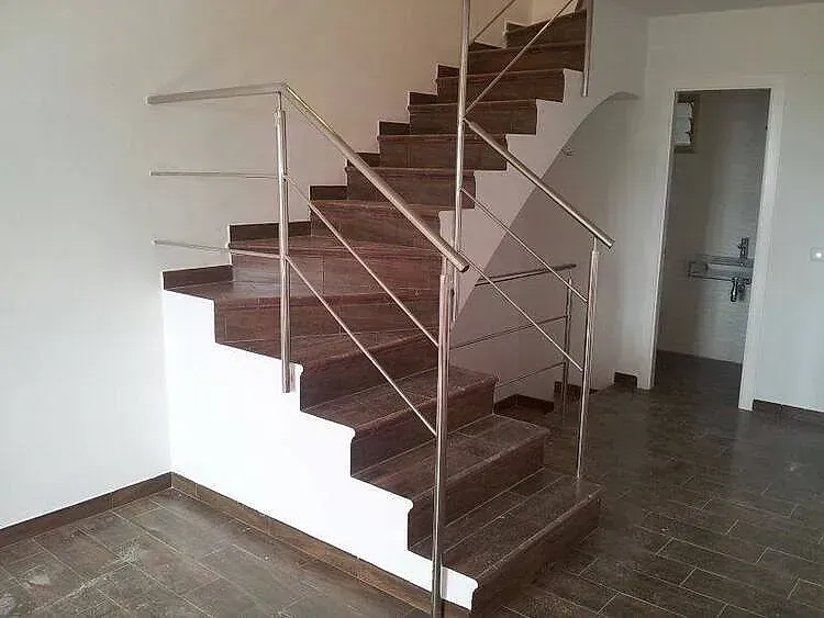 Escalera de caracol con escalones marrones y barandilla de metal en una habitación vacía con suelo de baldosas.
