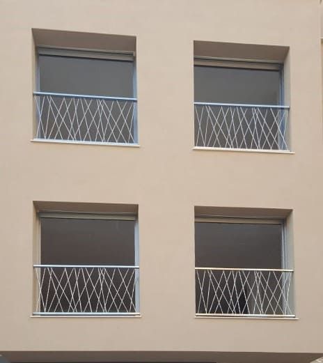 Fachada de edificio color beige con cuatro ventanas y rejas de seguridad blancas entrecruzadas.