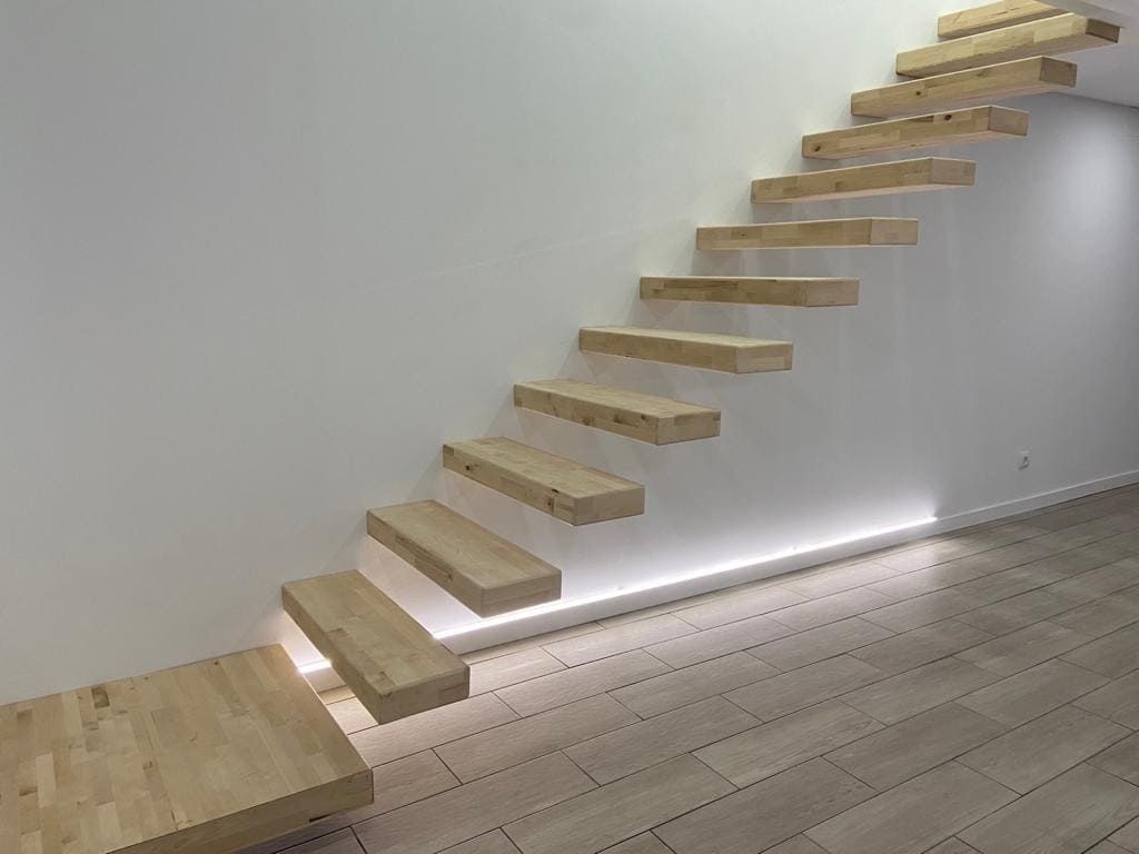 Escalera flotante de madera a lo largo de una pared blanca sobre un suelo de madera clara.