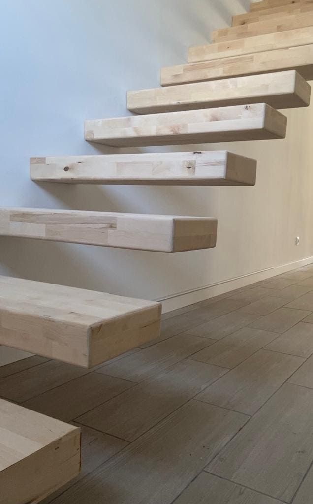 Escalera flotante de madera en un interior luminoso con paredes claras y suelo de baldosas.