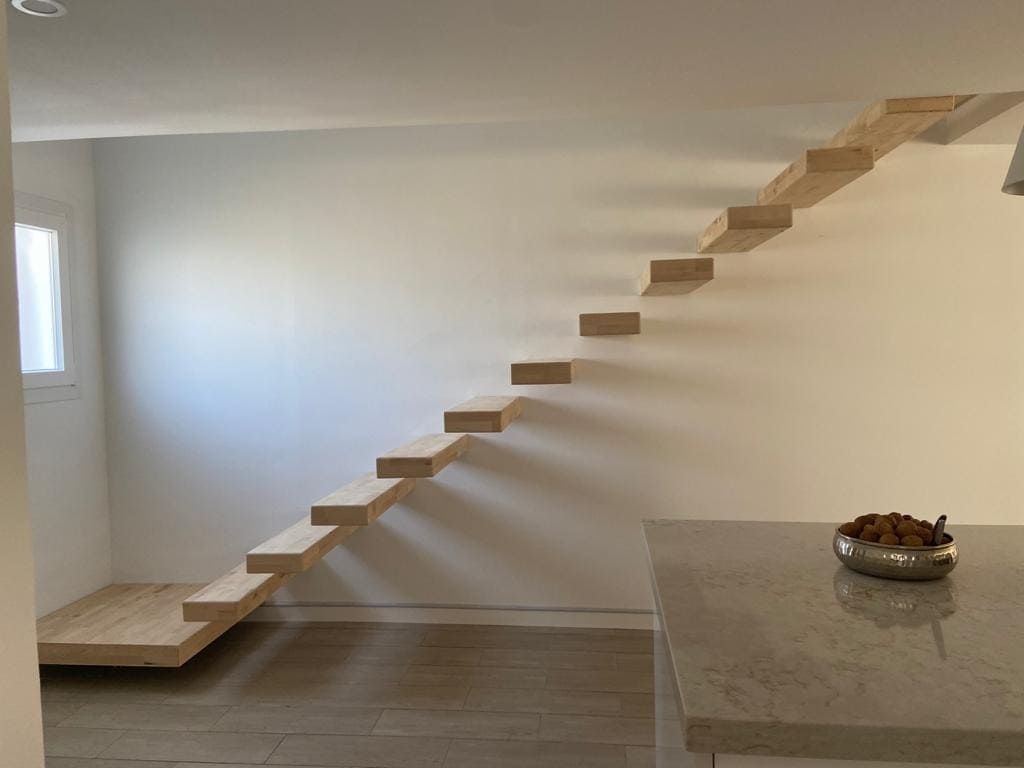 Interior minimalista con escaleras de madera flotantes y una pared blanca junto a la encimera de la cocina.