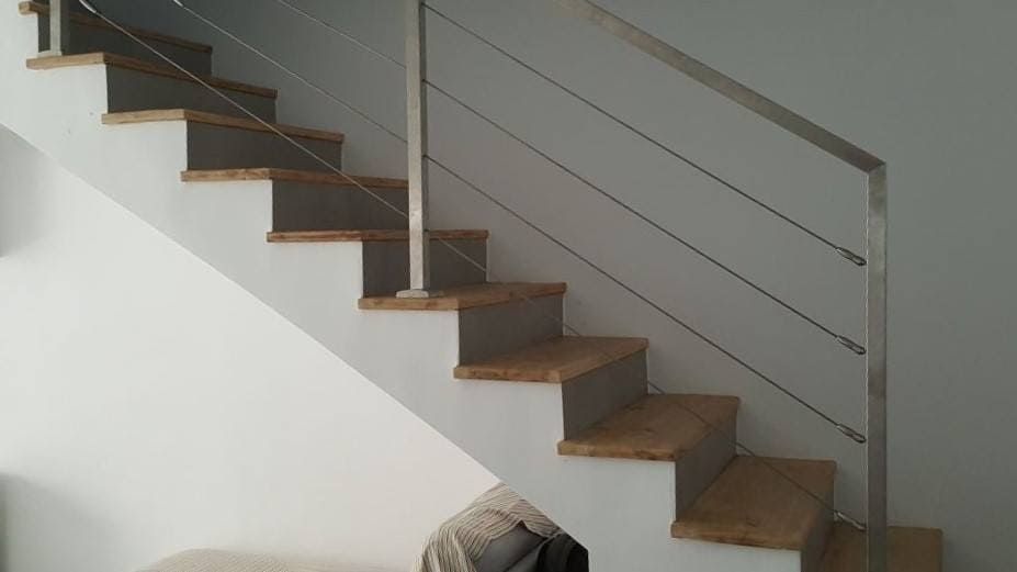 Escalera interior moderna con escalones de madera, barandilla de metal y paredes blancas.