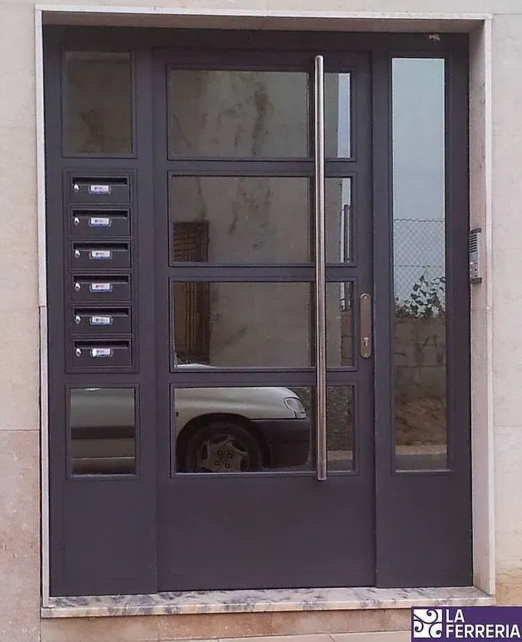 Puerta de entrada moderna de color gris oscuro para apartamento, con buzones y paneles laterales estrechos para las ventanas.