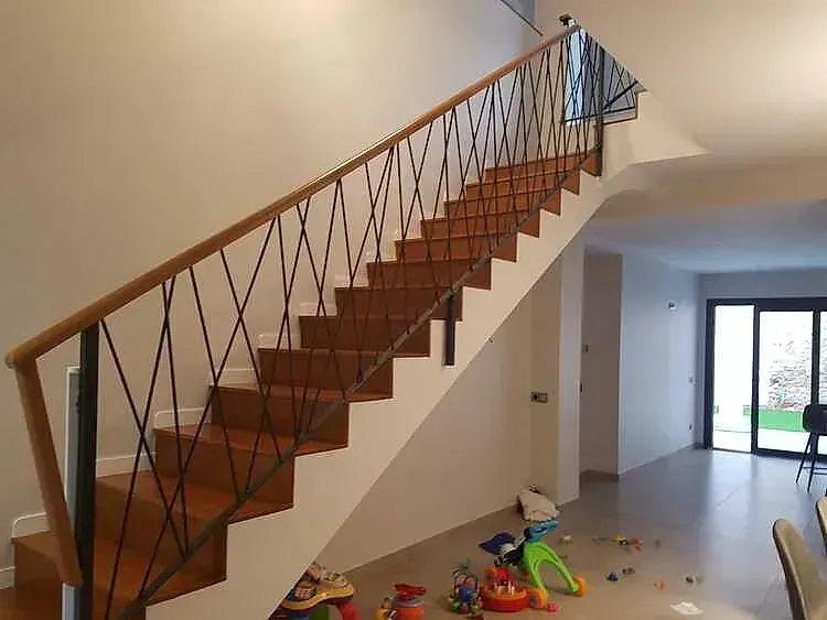 Escalera interior con peldaños y barandilla de madera, en una luminosa sala de estar con juguetes esparcidos por el suelo.