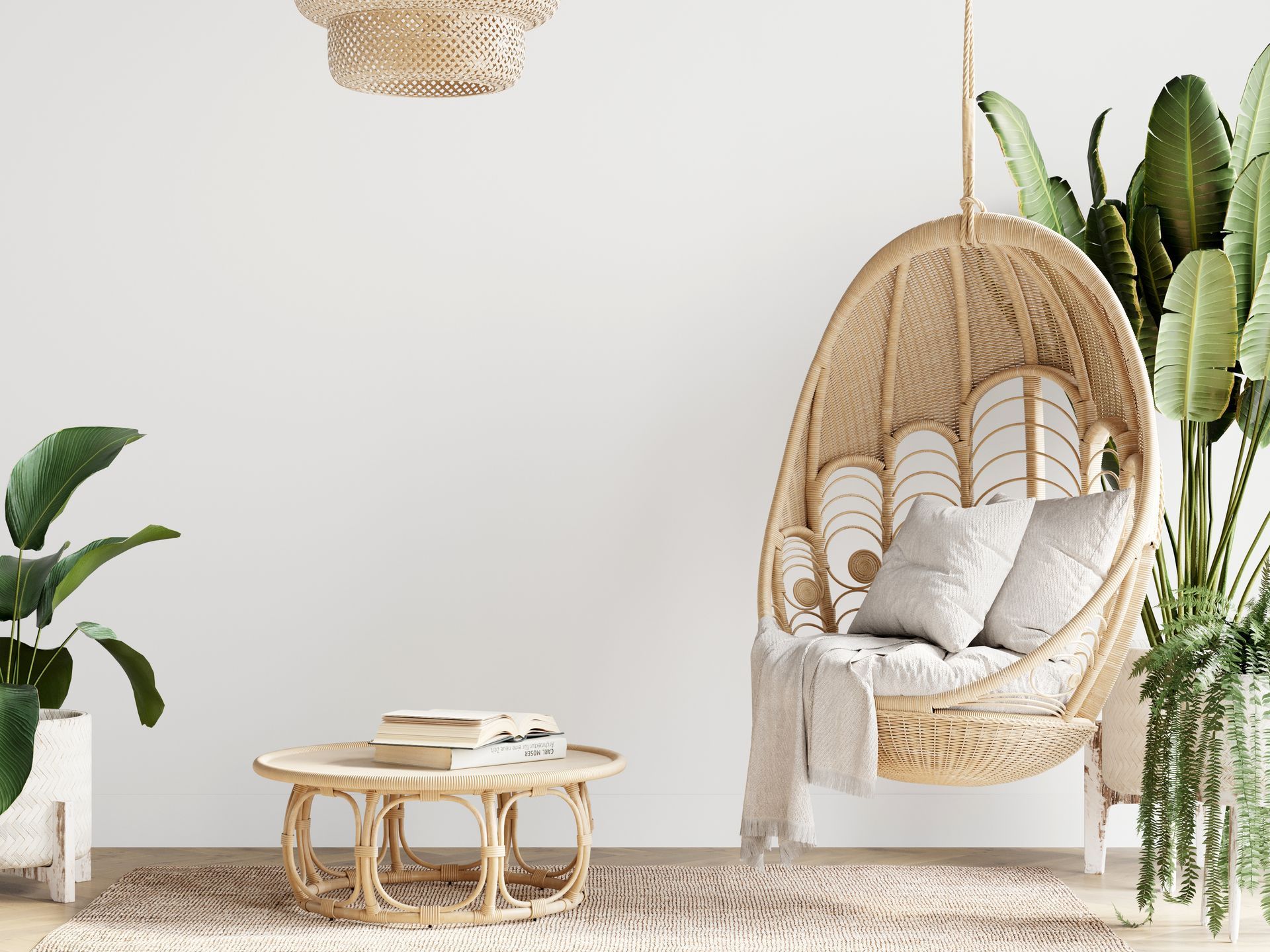 Salon de style bohème : fauteuil suspendu en osier avec coussins, petite table basse, plantes en pot, tapis et mur blanc.