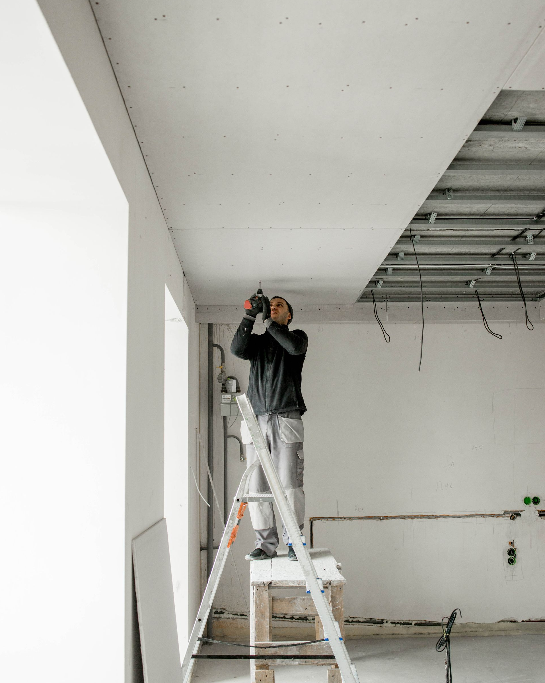 Un homme sur un escabeau en train de fixer des plaques de plâtre au plafond