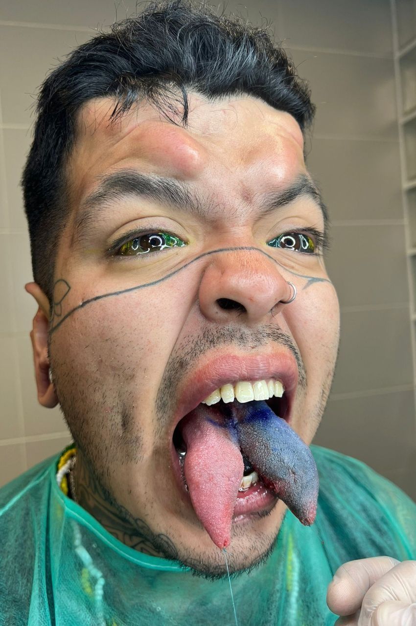 Un hombre con la cara pintada saca la lengua y se apunta con un cuchillo falso al espejo del baño.
