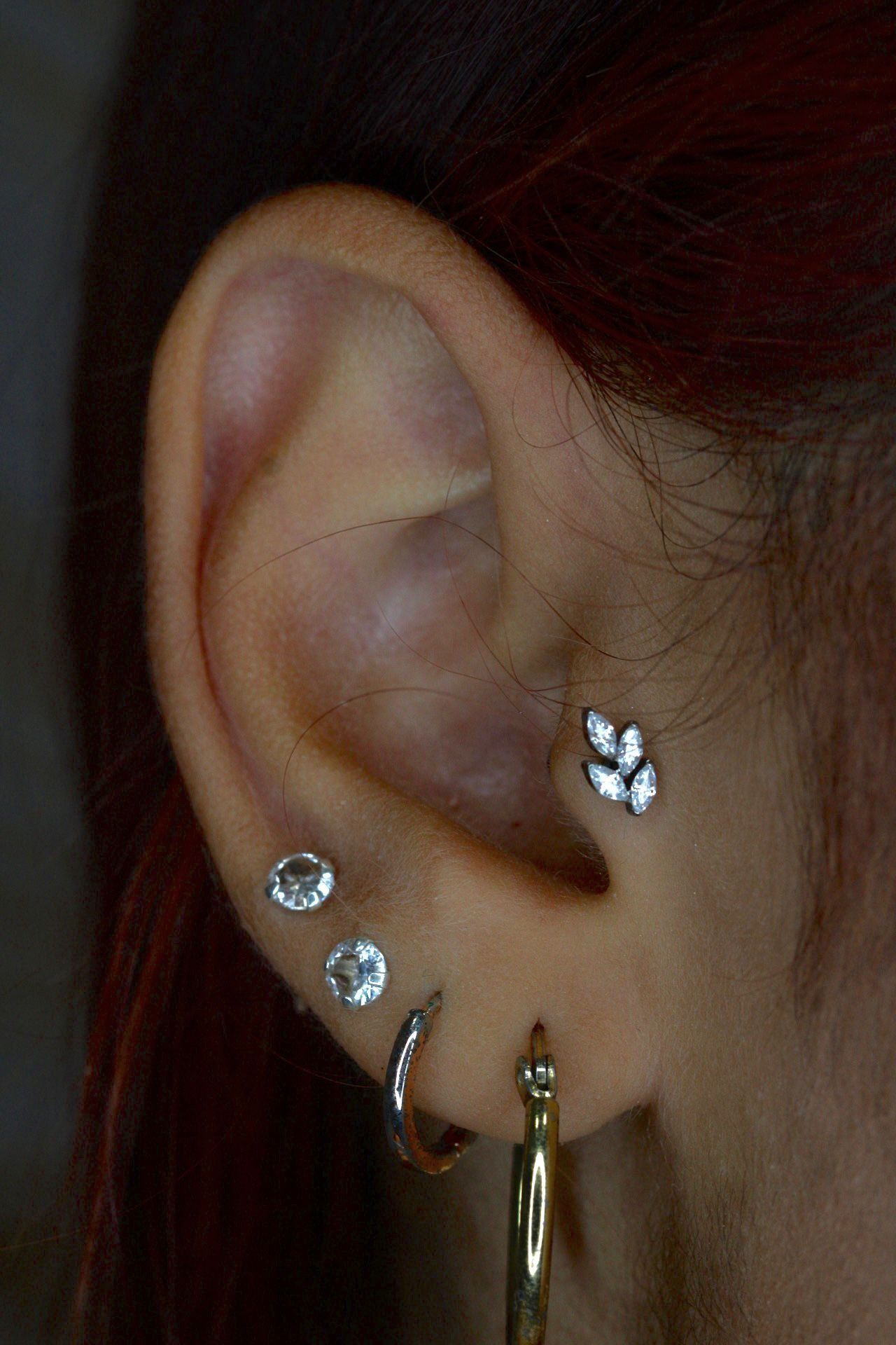 Primer plano de una oreja con varios pendientes de plata y un pequeño pendiente floral.