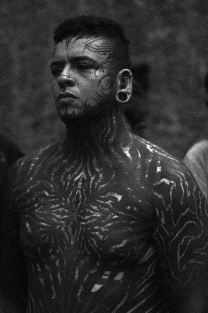 Retrato en blanco y negro de una persona tatuada con una joya estirada en el lóbulo de la oreja, mirando hacia la izquierda