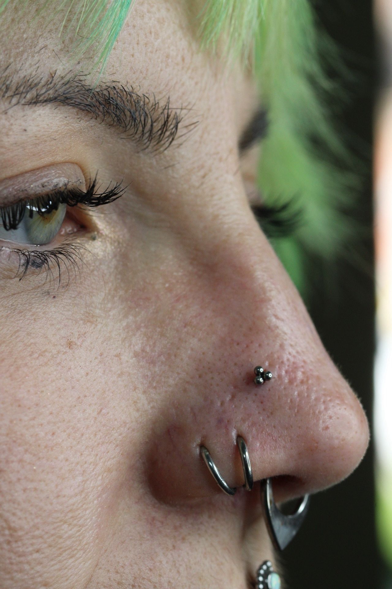 Primer plano de un rostro con cabello verde y múltiples piercings en la nariz.