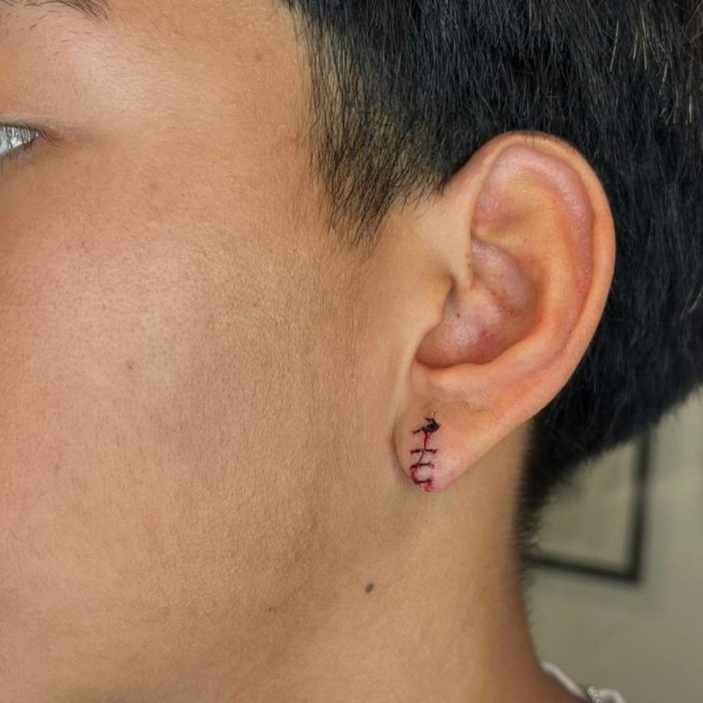 Primer plano de la oreja de una persona con un pequeño pendiente rosa con diseño bordado y cabello negro corto.