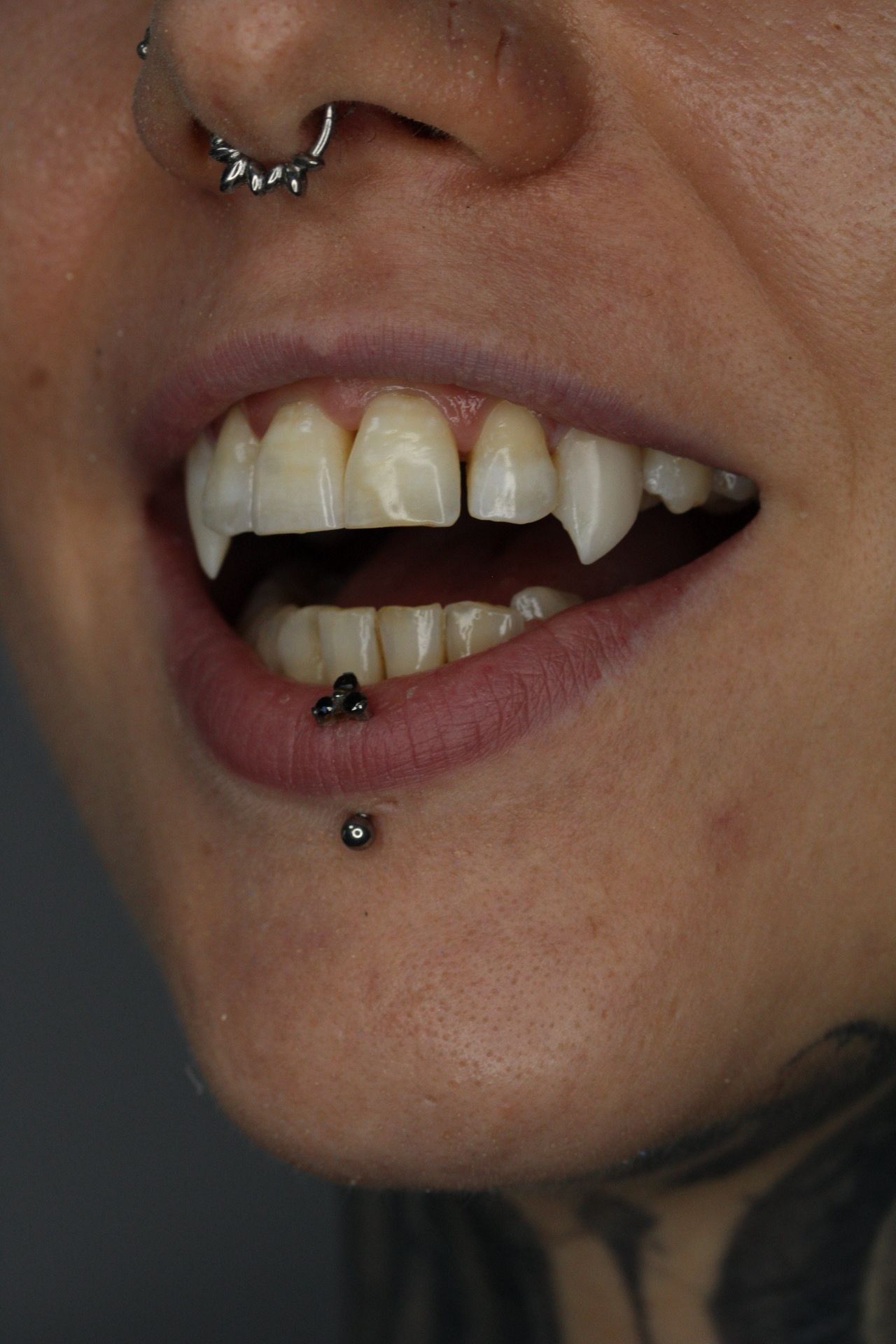 Primer plano de una persona con un piercing en la nariz y colmillos, con los labios entreabiertos en un estilo oscuro