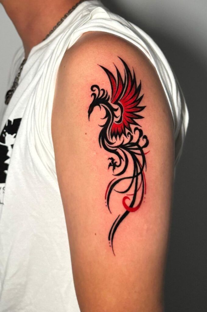 Tatuaje de un fénix negro y rojo en la parte superior del brazo de una persona, que se muestra sobre una camisa blanca.