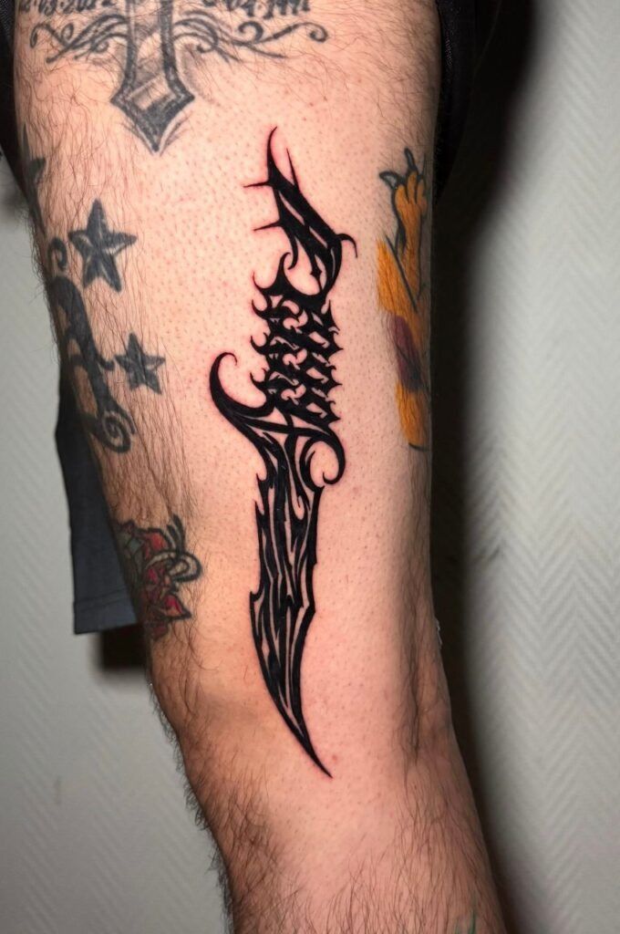 Antebrazo con un tatuaje negro en forma de llama y pequeños tatuajes de estrellas sobre piel clara.