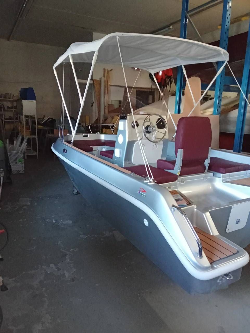 Motoscafo blu e bianco con tettuccio parcheggiato all'interno di un garage, con console di guida e sedili visibili.