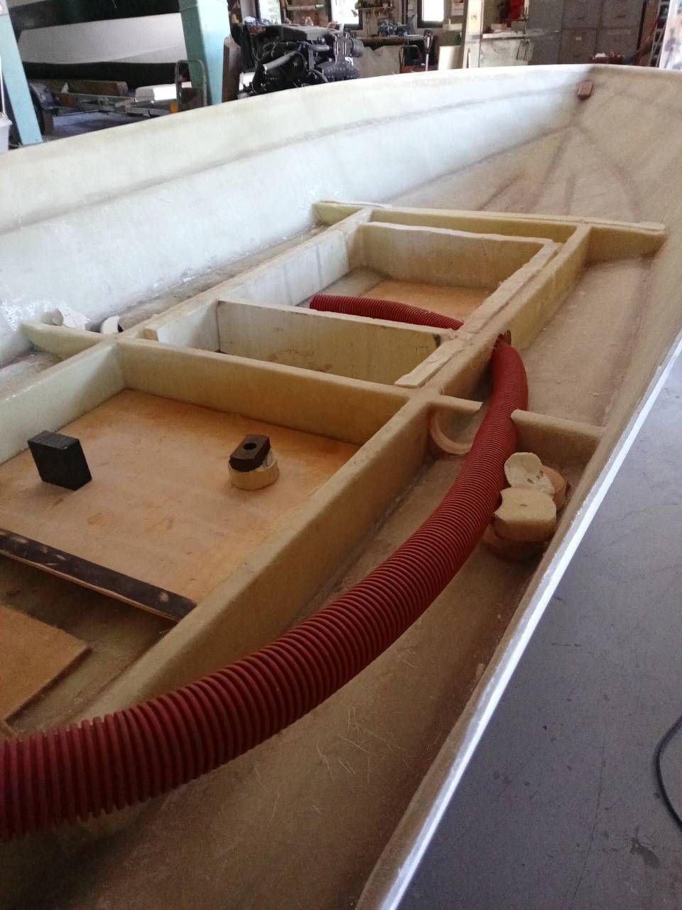 Interno di una barca in legno con un tubo rosso e attrezzi disposti in un'area di lavoro.