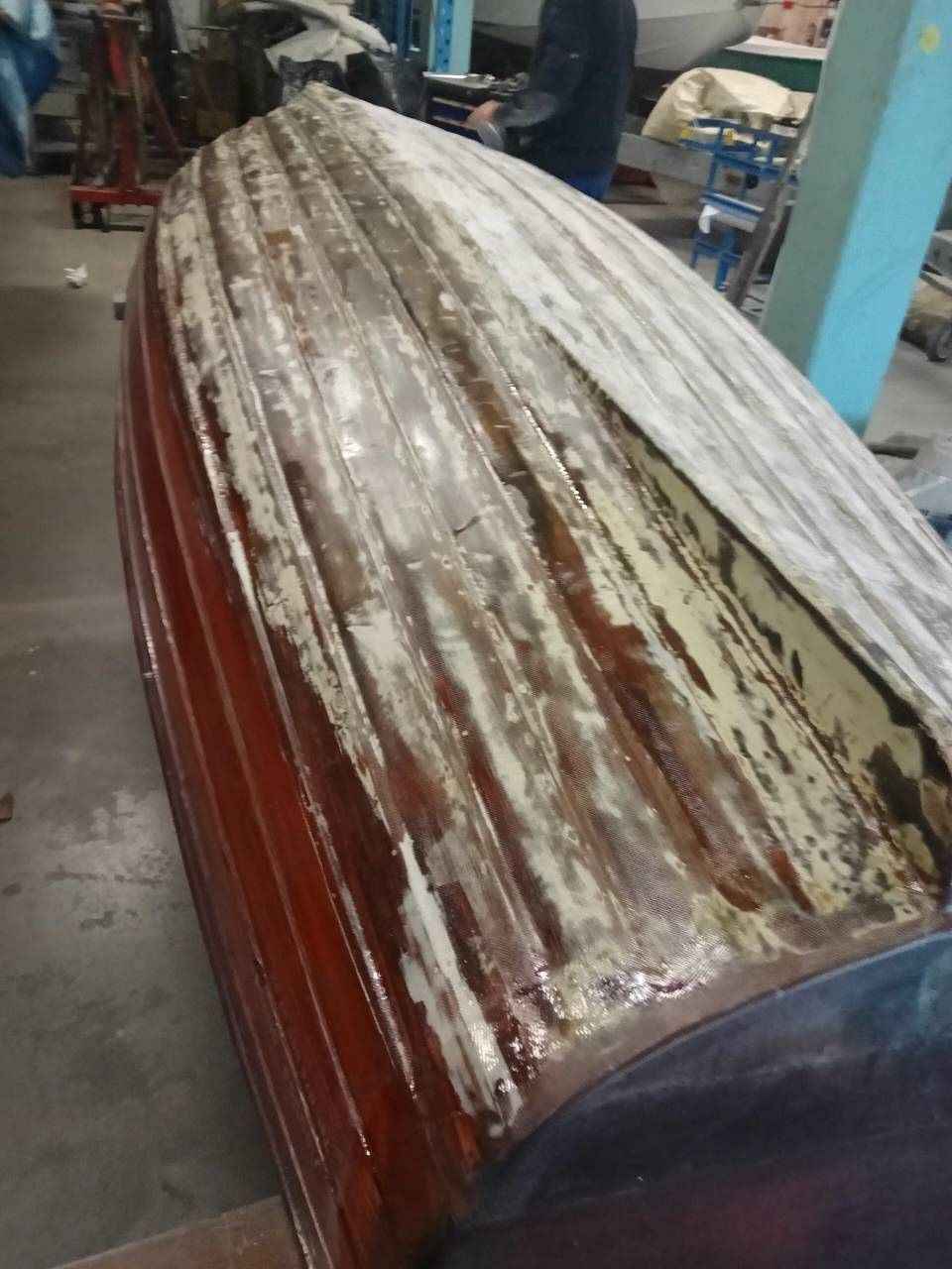 Scafo di barca in legno deteriorato con vernice bianca scrostata in un'officina