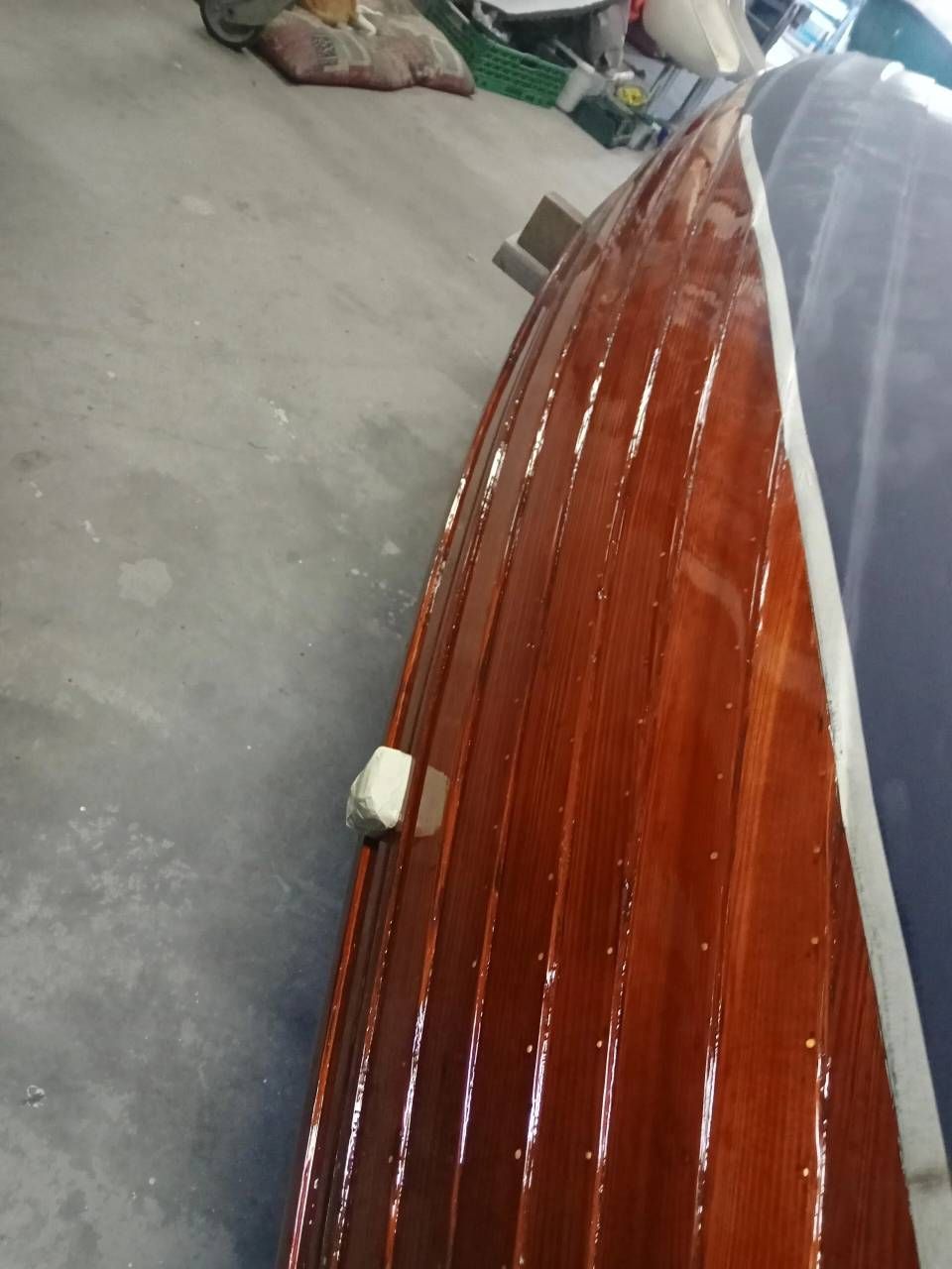 Primo piano di una superficie in legno lucido color marrone rossastro con finiture bianche sul pavimento di un'officina.