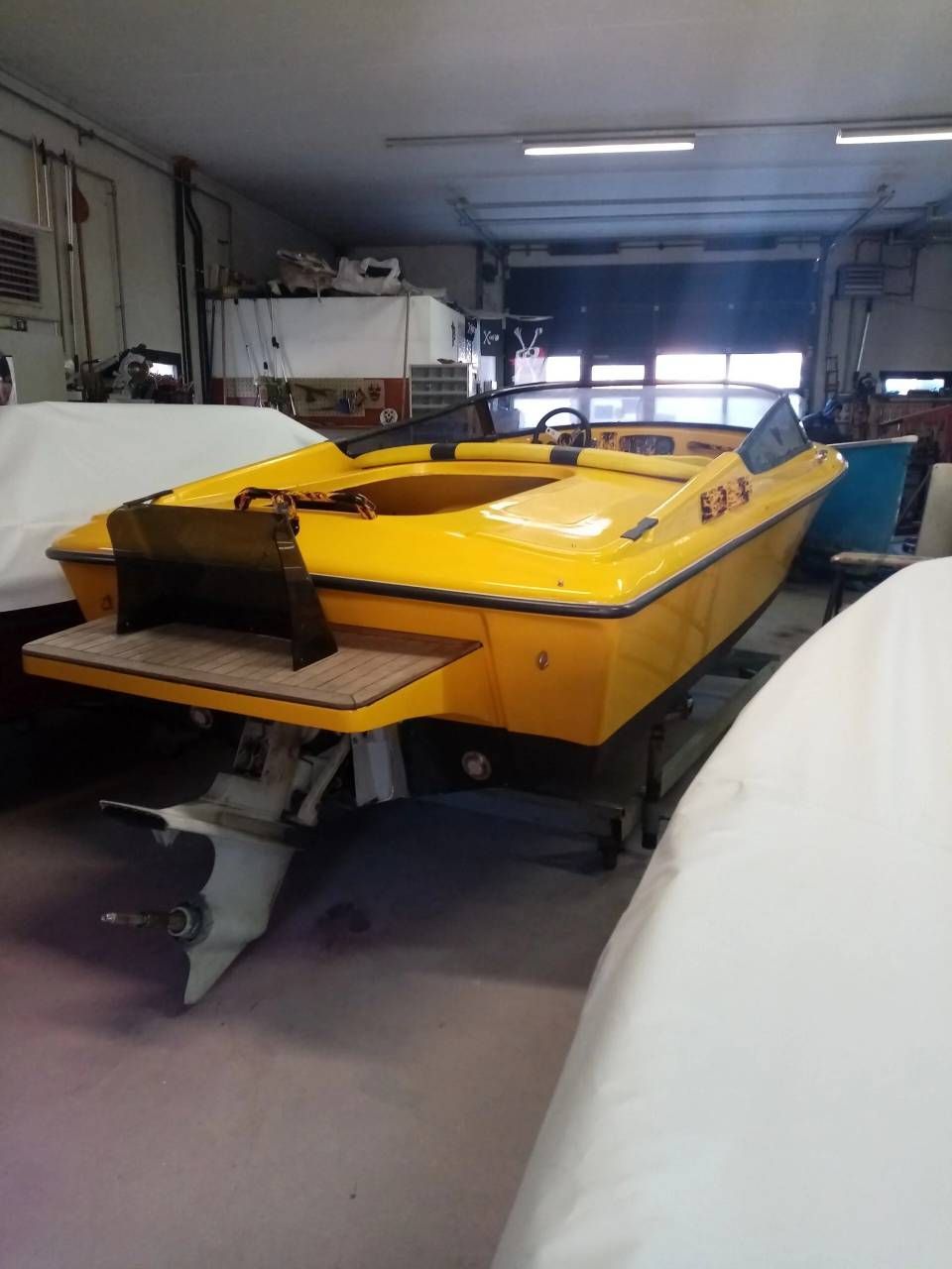 Motoscafo giallo su rimorchio all'interno di un garage, con ampia piattaforma posteriore e prua coperta.