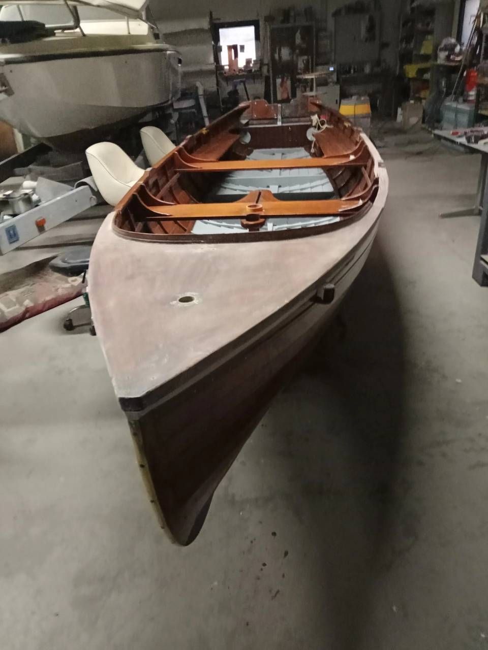 Barca a remi in legno con scafo bianco e prua scura, mostrata all'interno di un'officina o di una rimessa per barche.