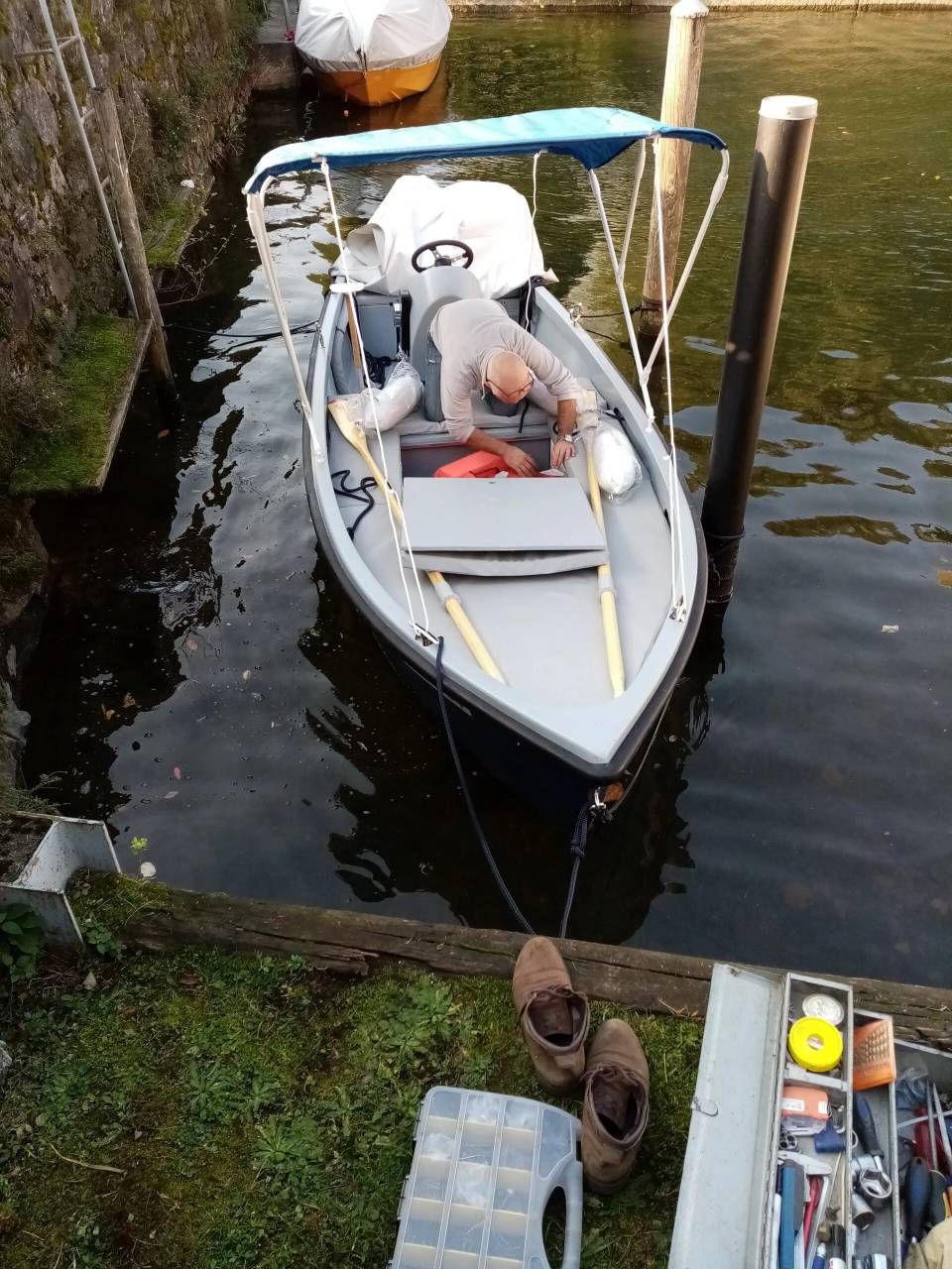 Una piccola imbarcazione a motore bianca è ormeggiata in un canale, accanto a un molo di legno e a una sponda erbosa.