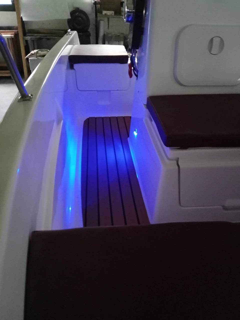 Corridoio illuminato di blu all'interno dell'abitacolo di un veicolo moderno, con sedili bianchi e uno stretto passaggio.