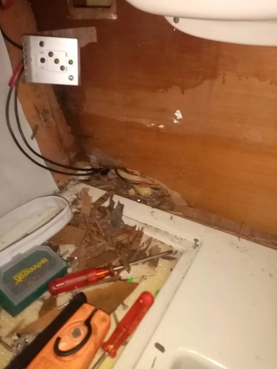 Angolo ingombro di fili scoperti, presa a muro, attrezzi e detriti sul pavimento.
