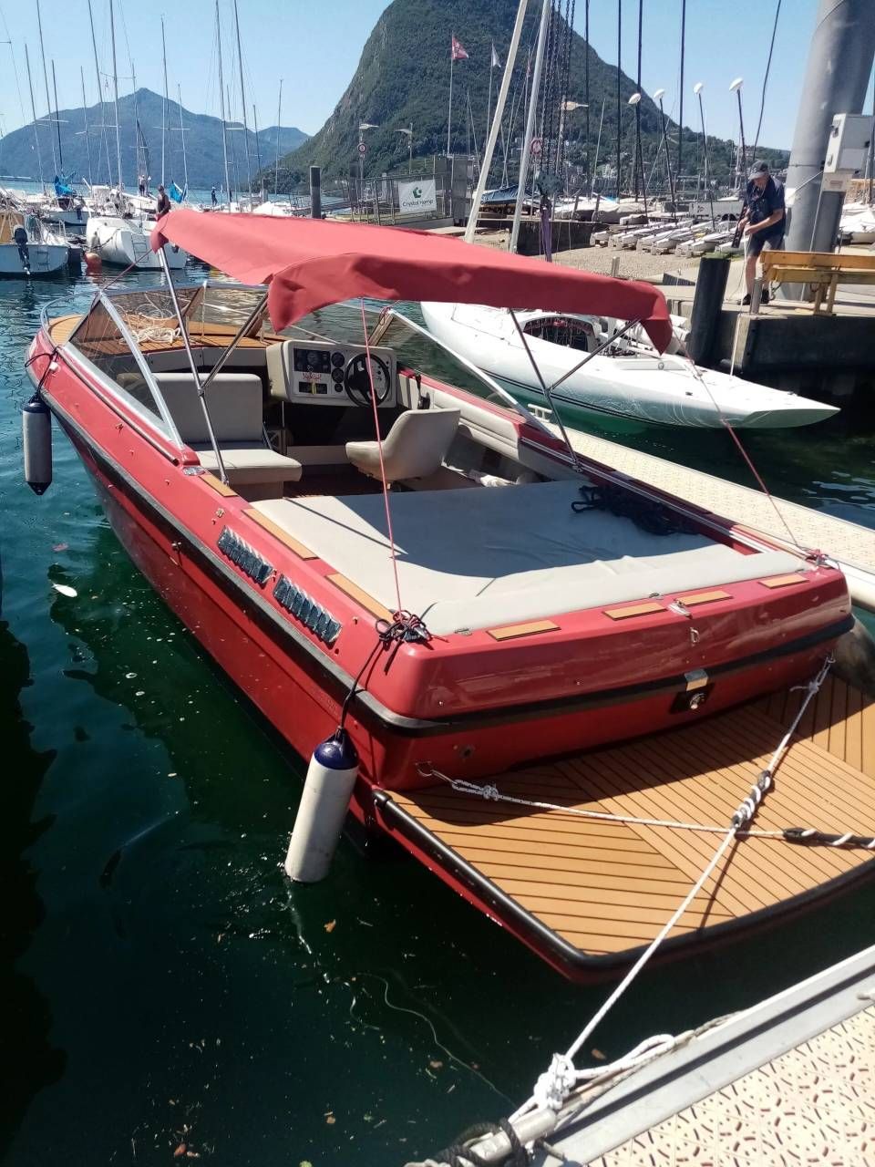 Motoscafo rosso con tettuccio rosso ormeggiato in un porticciolo accanto ad altre barche e alberi di barche a vela.