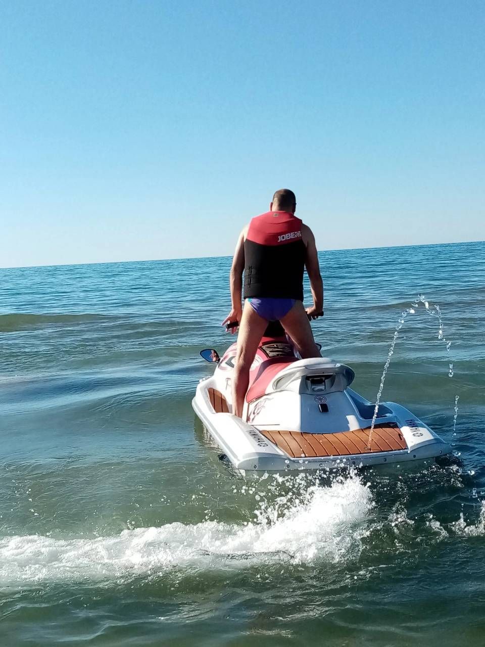 Una persona a bordo di una moto d'acqua sull'oceano, con indosso un giubbotto di salvataggio rosso, lascia dietro di sé una scia.