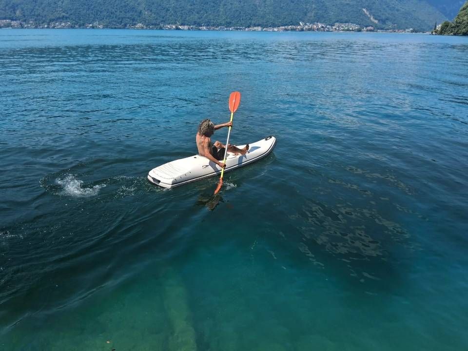 Una persona pagaia su un kayak bianco su acque cristalline, con montagne sullo sfondo.