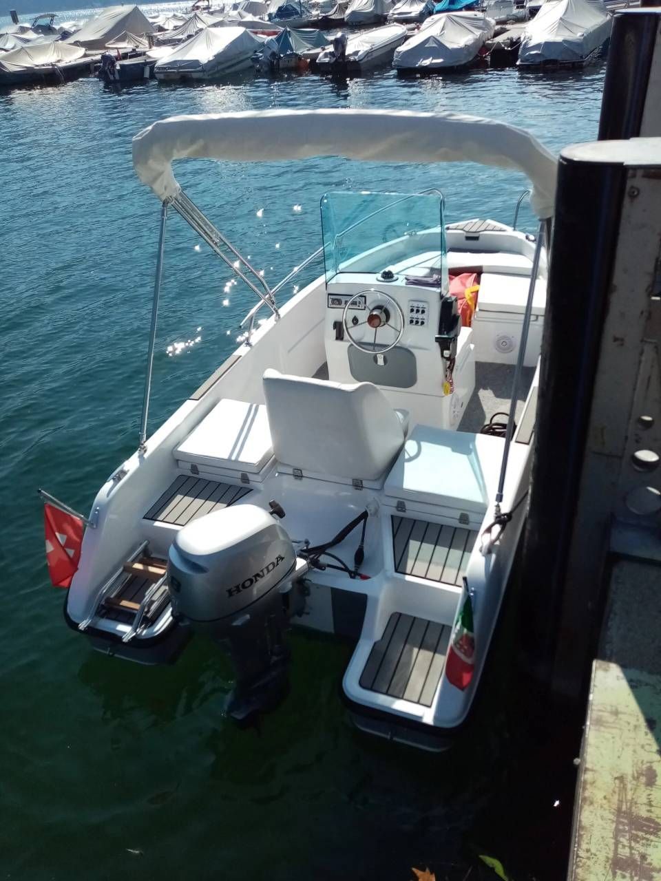 Piccola imbarcazione a motore bianca ormeggiata a un molo di pietra su acque azzurre con una costa rocciosa sullo sfondo.
