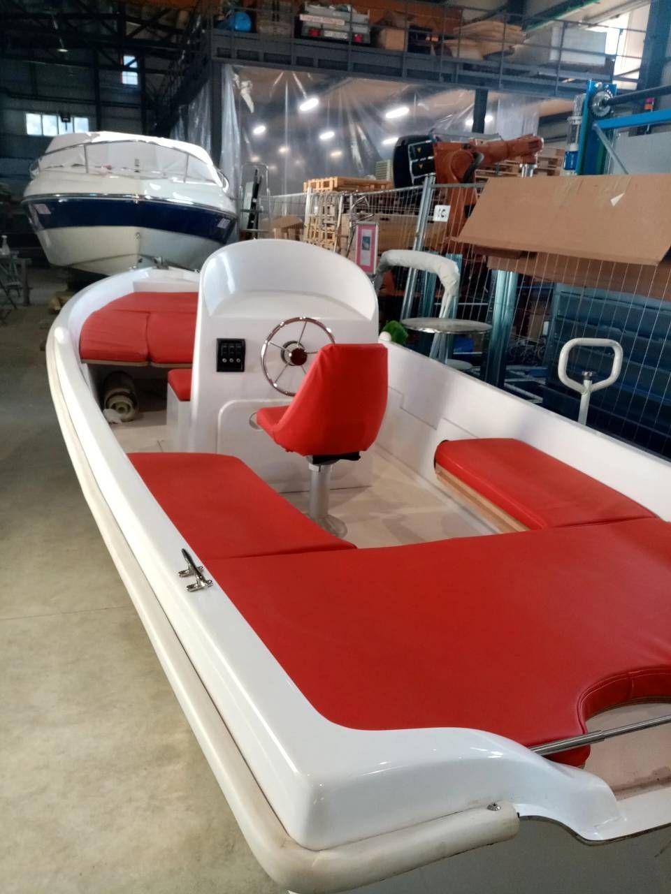 Interno di un motoscafo bianco e rosso in un cantiere navale, con consolle di guida e sedili imbottiti.