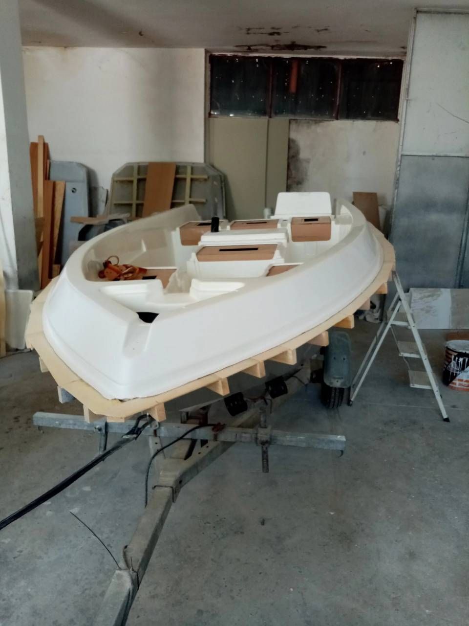 Scafo di barca bianco parzialmente costruito in un'officina, con attrezzi e materiali intorno.