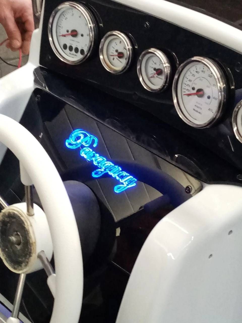 Cruscotto dell'auto con quattro indicatori, volante bianco e scritta al neon blu su un pannello nero