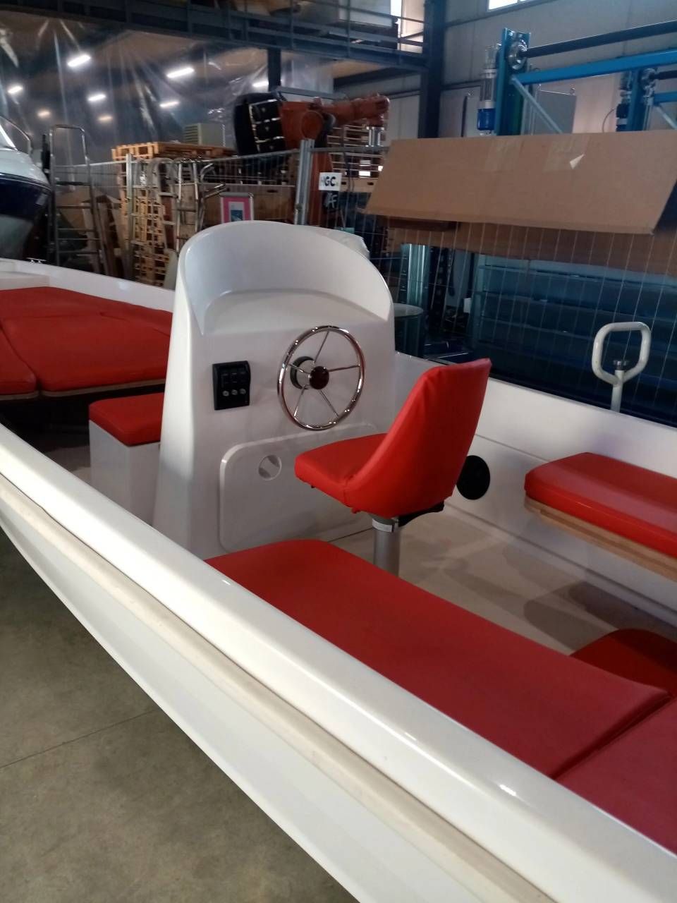 Abitacolo di una barca rosso e bianco con volante e sedili in un'officina o in un porto turistico.