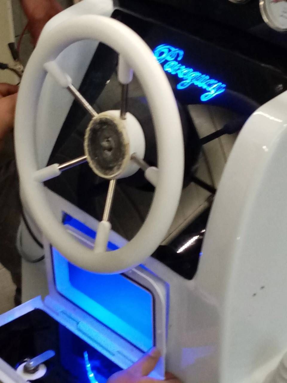 Macchina arcade bianca a forma di ruota con apertura illuminata di blu e una mano che preme un pulsante.