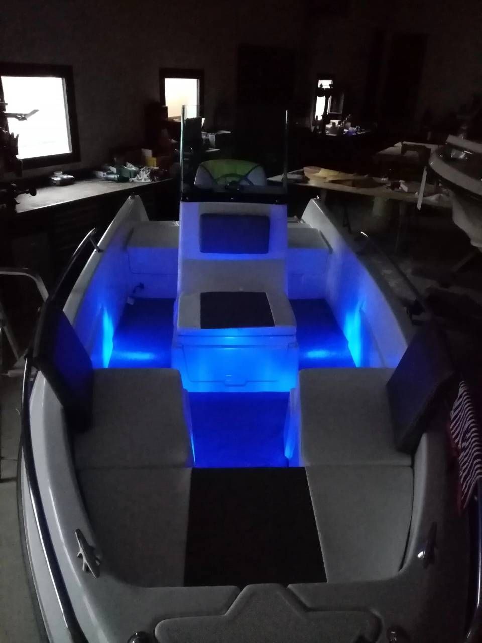 Cabina di una piccola imbarcazione con illuminazione a LED blu e sedili grigi, vista da poppa.