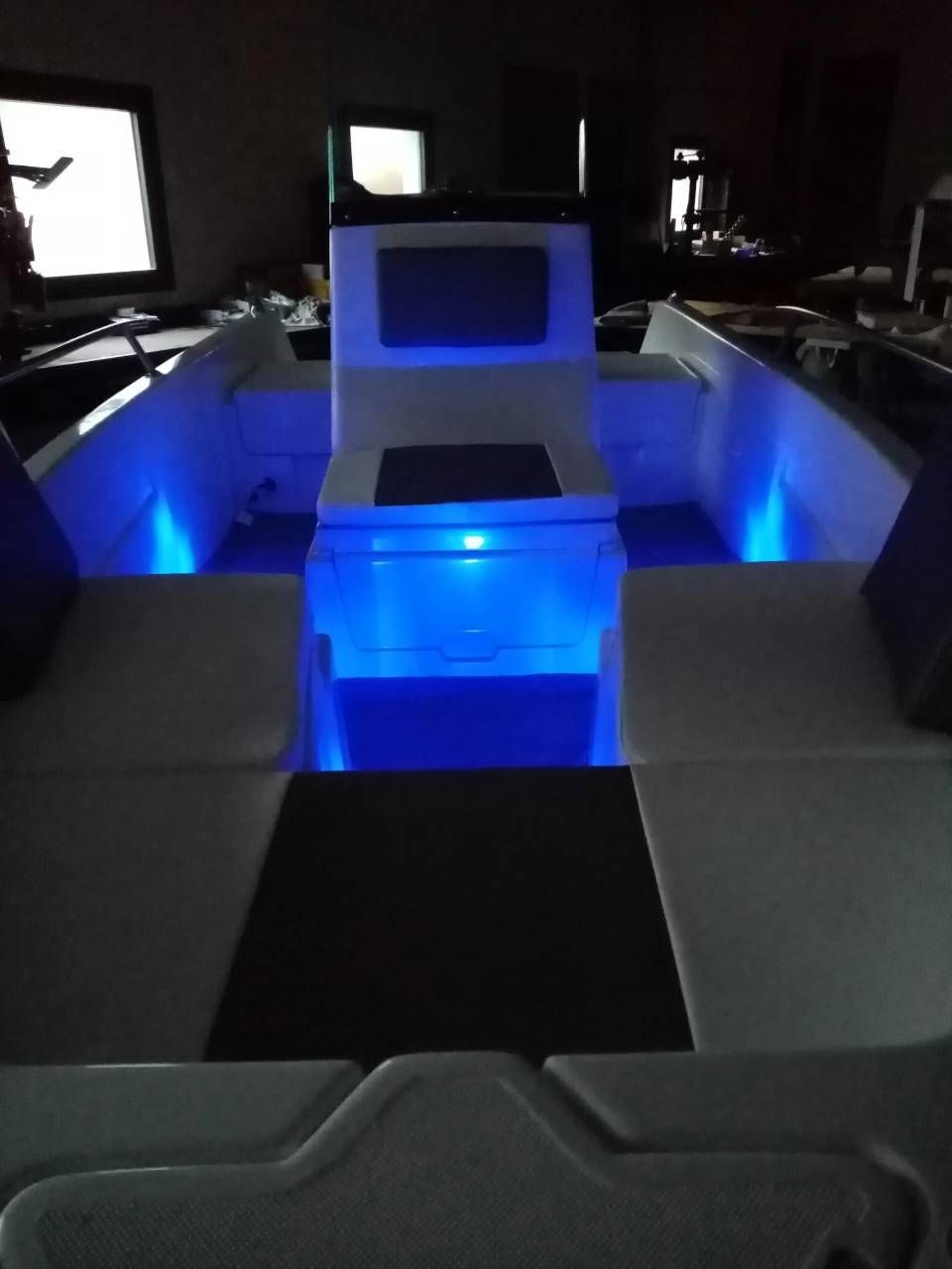Cabina di una barca scarsamente illuminata con sedili illuminati da LED blu e un tavolo centrale.